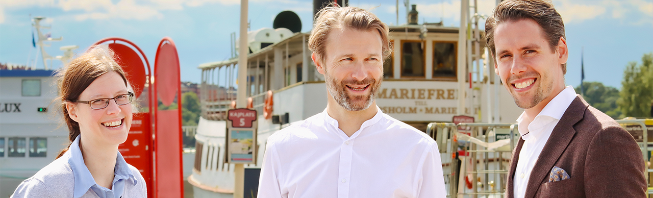 [Translate to English:] Fotografie von drei Personen vor einem Hafenschiff